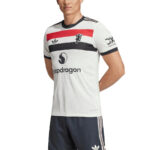 Man wearing a white football jersey with red and black horizontal bands, crest on chest, and sponsor logos (Snapdragon) while posing in dark shorts.