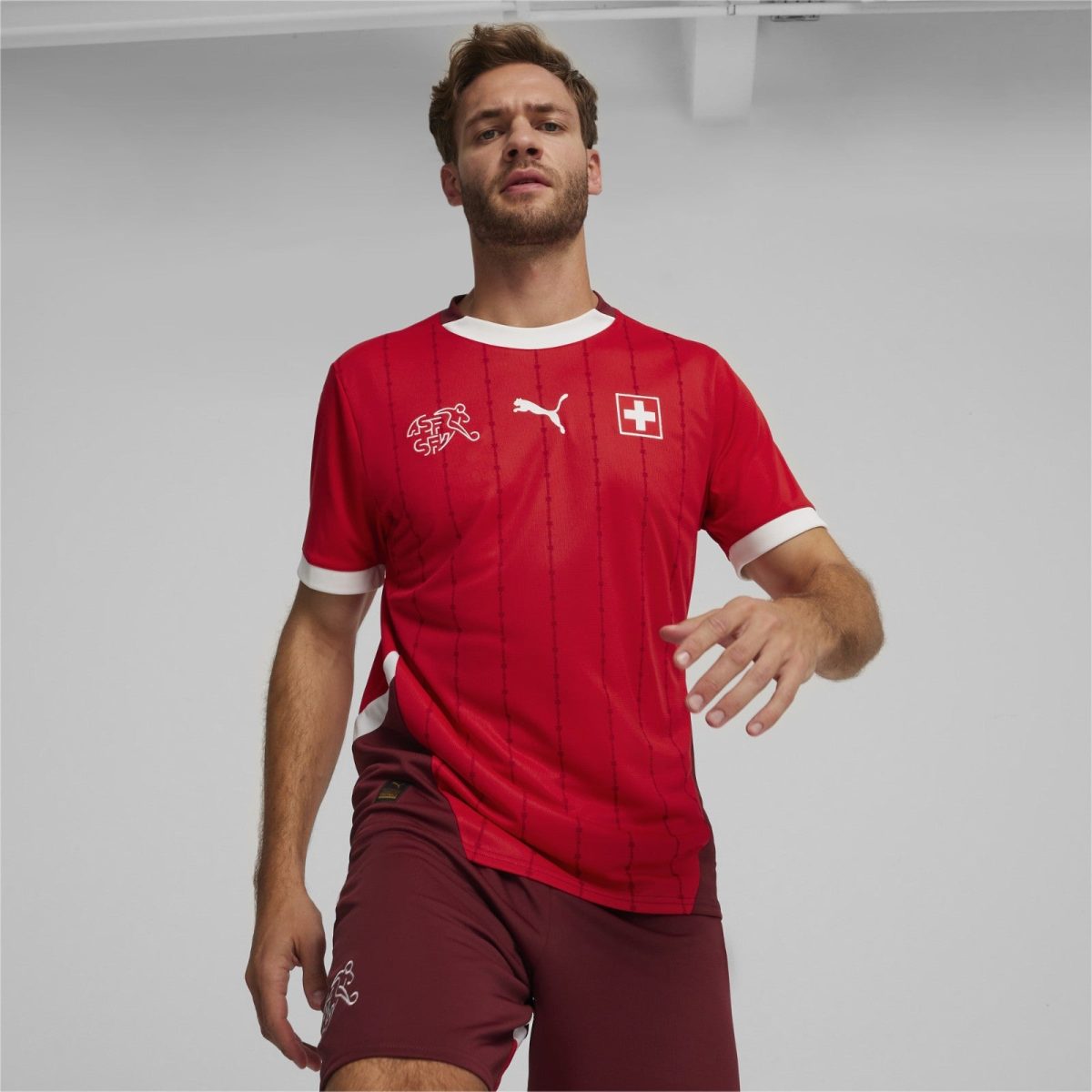 Male model wearing a red Swiss football jersey with white trim and logos, posed against a light gray background.