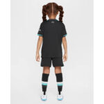 Back view of a young girl wearing a black soccer kit with teal trim, black shorts, LFC socks, and white cleats.