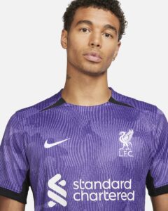 liverpool-third-jersey-202324-333525_8311464c-360b-43da-a4b8-c54b56393471 | UAE SPORT STORE Close-up of a person wearing a purple Liverpool FC training jersey with the Standard Chartered logo on the chest