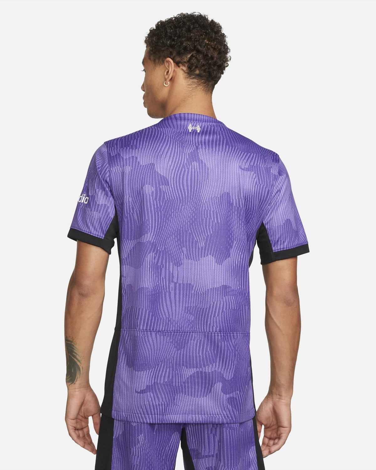 Back view of a person wearing a purple camo-pattern athletic jersey with black side panels, short sleeves, and a small logo at the neck.