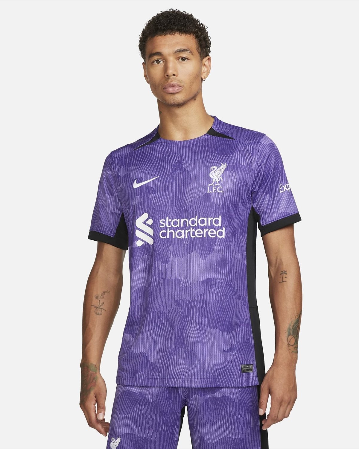 Man modeling a purple Liverpool FC football jersey with Standard Chartered logo, front view against a light background.