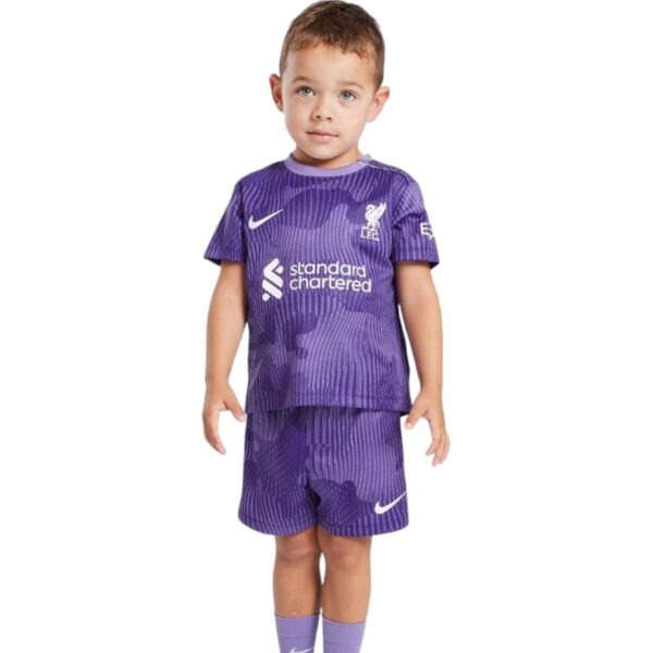 A young boy wearing a purple Liverpool FC soccer kit (shirt and shorts) with sponsor logo and Nike swoosh, standing against a white background.