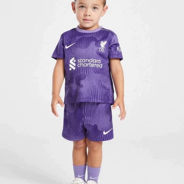 Toddler wearing a purple Liverpool FC soccer kit (jersey and shorts) with white sneakers, standing against a light background.