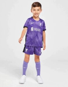 Young boy wearing a purple Liverpool FC youth kit with shorts and socks, posing against a light background.