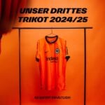 lixq8d9CMx9DLo9 | UAE SPORT STORE Orange football jersey hanging on a rack against an orange wall, with bold German text about the 2024/25 third kit and availability at the bottom.