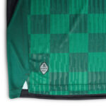 lkj | UAE SPORT STORE Green plaid fabric of a garment hem with a small circular badge that reads 'Authentic Product' near the hem.