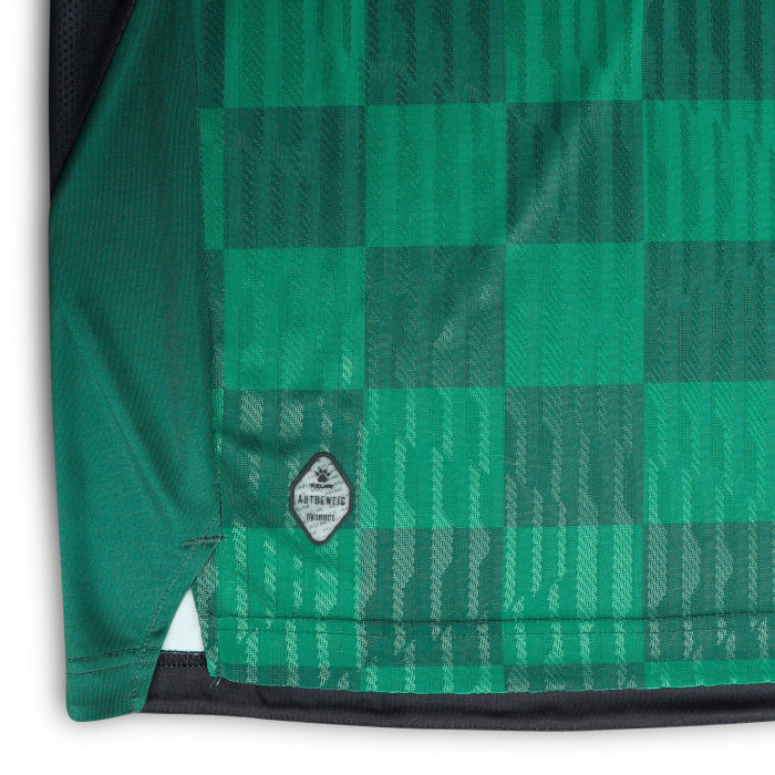 lkj | UAE SPORT STORE Green plaid fabric of a garment hem with a small circular badge that reads 'Authentic Product' near the hem.