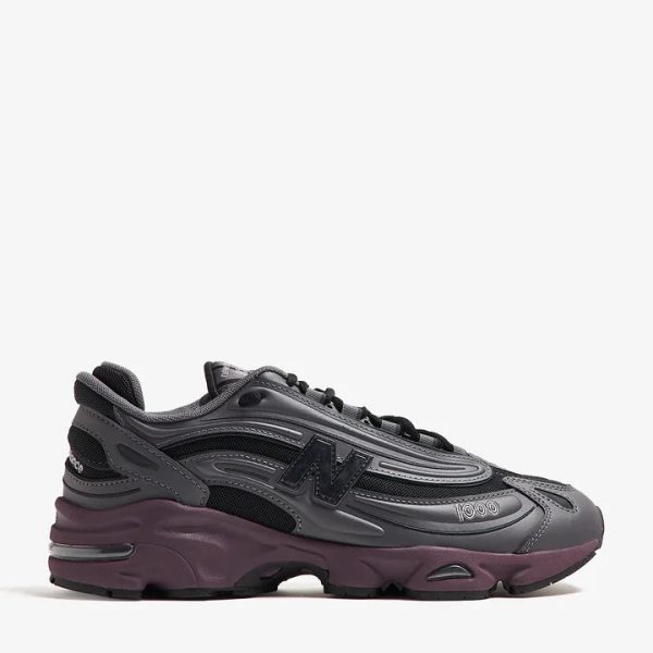Dark gray/black chunky athletic sneaker with a purple-maroon sole on a white background, side view emphasizing layered panels.
