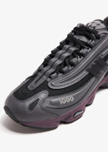 m1000eb-052_5 | UAE SPORT STORE Close-up of a dark gray athletic sneaker with black mesh panels, laces, and a purple-tinted sole showing '1000' on the side.