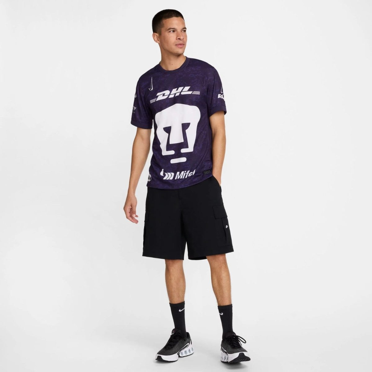 Model wearing a purple graphic t-shirt with DHL logo and black cargo shorts, standing against a white backdrop.