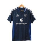 Dark blue Manchester United soccer jersey on a wooden hanger, featuring Adidas logo and Snapdragon sponsor text on front.