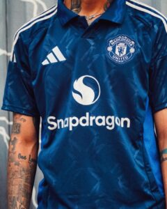Man United blue jersey with Snapdragon sponsor and club crest visible on chest, partial tattoos on arms
