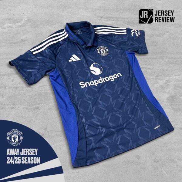 Manchester United away jersey in blue with white Adidas stripes, Snapdragon sponsor, laid flat on a gray surface.