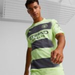 Male model wearing a neon green and dark gray Manchester City jersey, facing the camera.