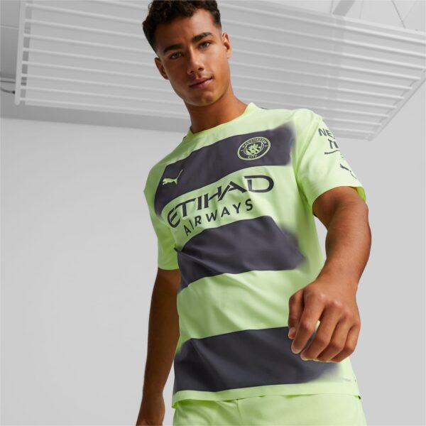 Male model wearing a neon green and dark gray Manchester City jersey, facing the camera.
