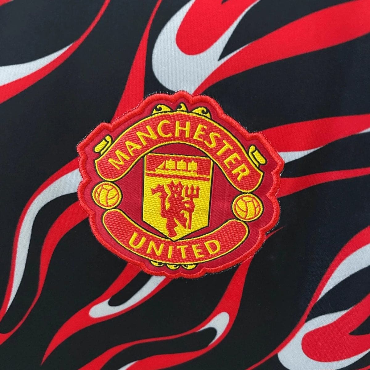Manchester United crest embroidered on a red-yellow badge against a red-and-black flame-pattern background