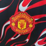 Manchester United crest embroidered on a red-yellow badge against a red-and-black flame-pattern background