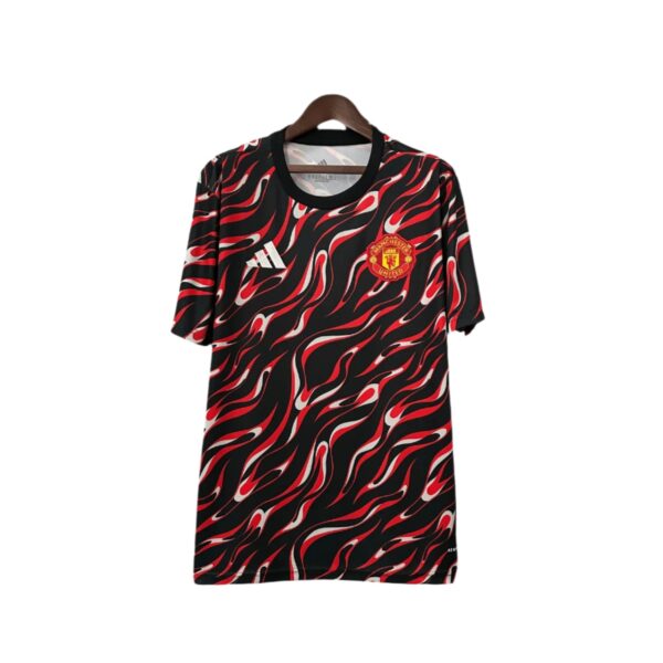 Black Manchester United jersey with red-white flame pattern, crest on the chest, hanging on a wooden hanger of a store display (informative).