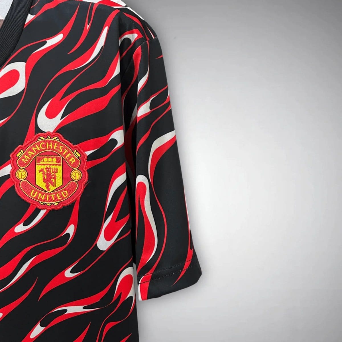 Close-up of a Manchester United jersey featuring a red flame pattern on black fabric with the club crest visible.