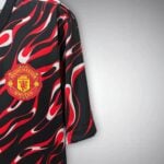 Close-up of a Manchester United jersey featuring a red flame pattern on black fabric with the club crest visible.
