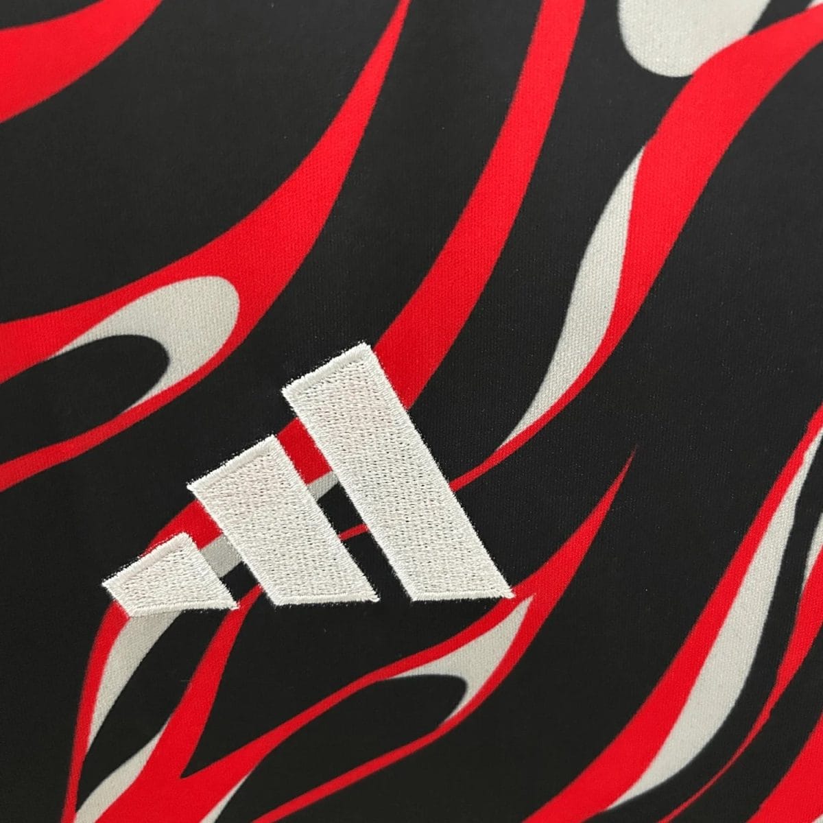 Close-up of white embroidered Adidas three-stripe logo on black fabric with red curved graphic(s).