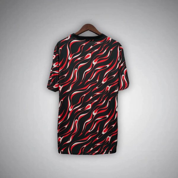Black dress with a red and white flame pattern hanging on a wooden hanger against a gray background.