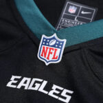 Close-up of a Philadelphia Eagles jersey with an NFL shield pin on teal collar, and 'EAGLES' text.
