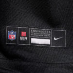Clothing label showing NFL logo, NFLPA symbol, and Nike swoosh with the caption 'Engineered to the exact specifications of championship athletes' on black fabric.