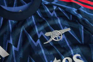 Close-up of a dark blue patterned sports jersey with a silver circular emblem featuring a wheel and wings near the chest area.