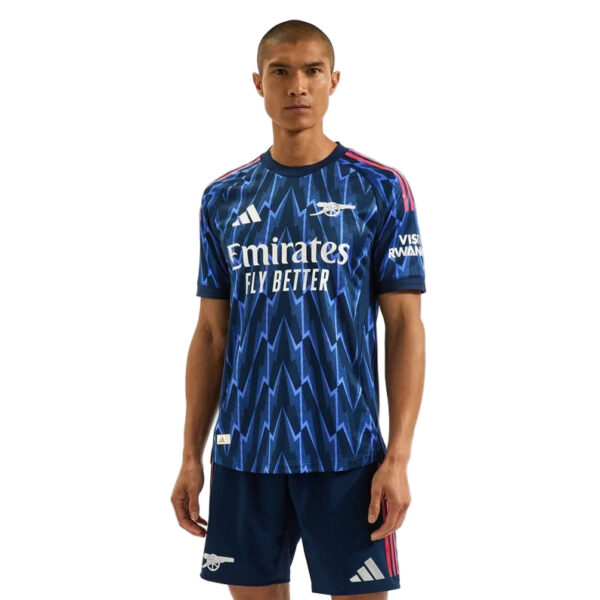 Male model wearing a blue Arsenal football away jersey with a zigzag pattern and Emirates Fly Better sponsor.