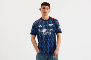 Man wearing a blue Arsenal football jersey with 'Emirates Fly Better' text, standing against a plain background.