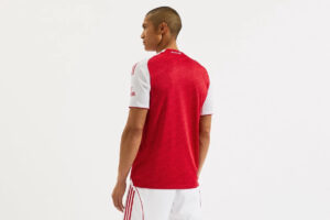 Back view of a man wearing a red soccer jersey with white sleeves.