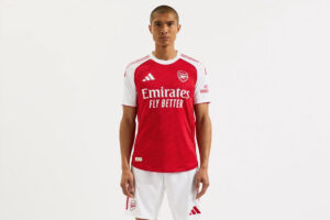 Front view of a man wearing an Arsenal red home football kit with white sleeves and white shorts.