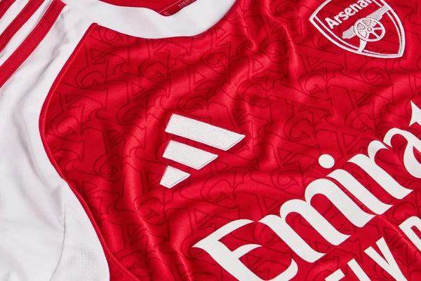 mji9536_d1 | UAE SPORT STORE Close-up of a red Arsenal FC jersey featuring the club crest and the white Emirates sponsor logo with white sleeve trim.