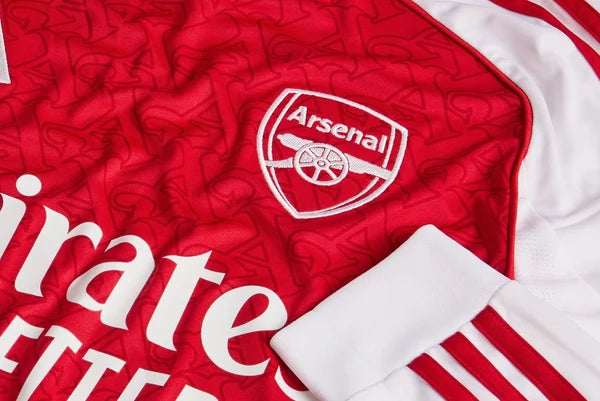 mji9536_d2 | UAE SPORT STORE Close-up of an Arsenal football jersey showing the club crest and white sponsor lettering on red fabric.