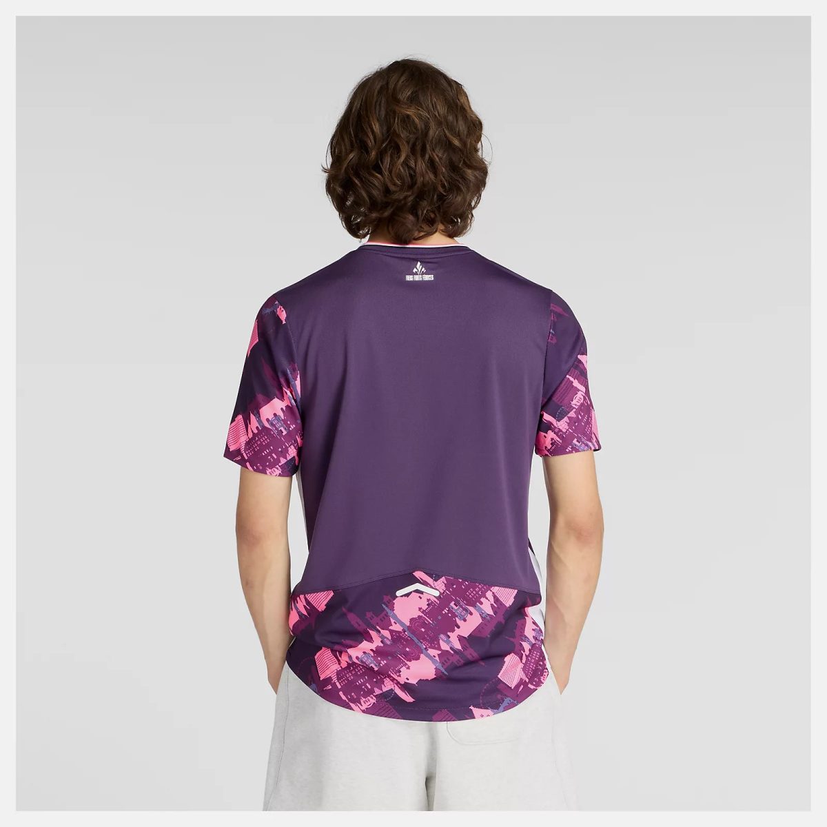 Back view of a person wearing a purple athletic jersey with pink abstract pattern on the sleeves and hem, gray background.