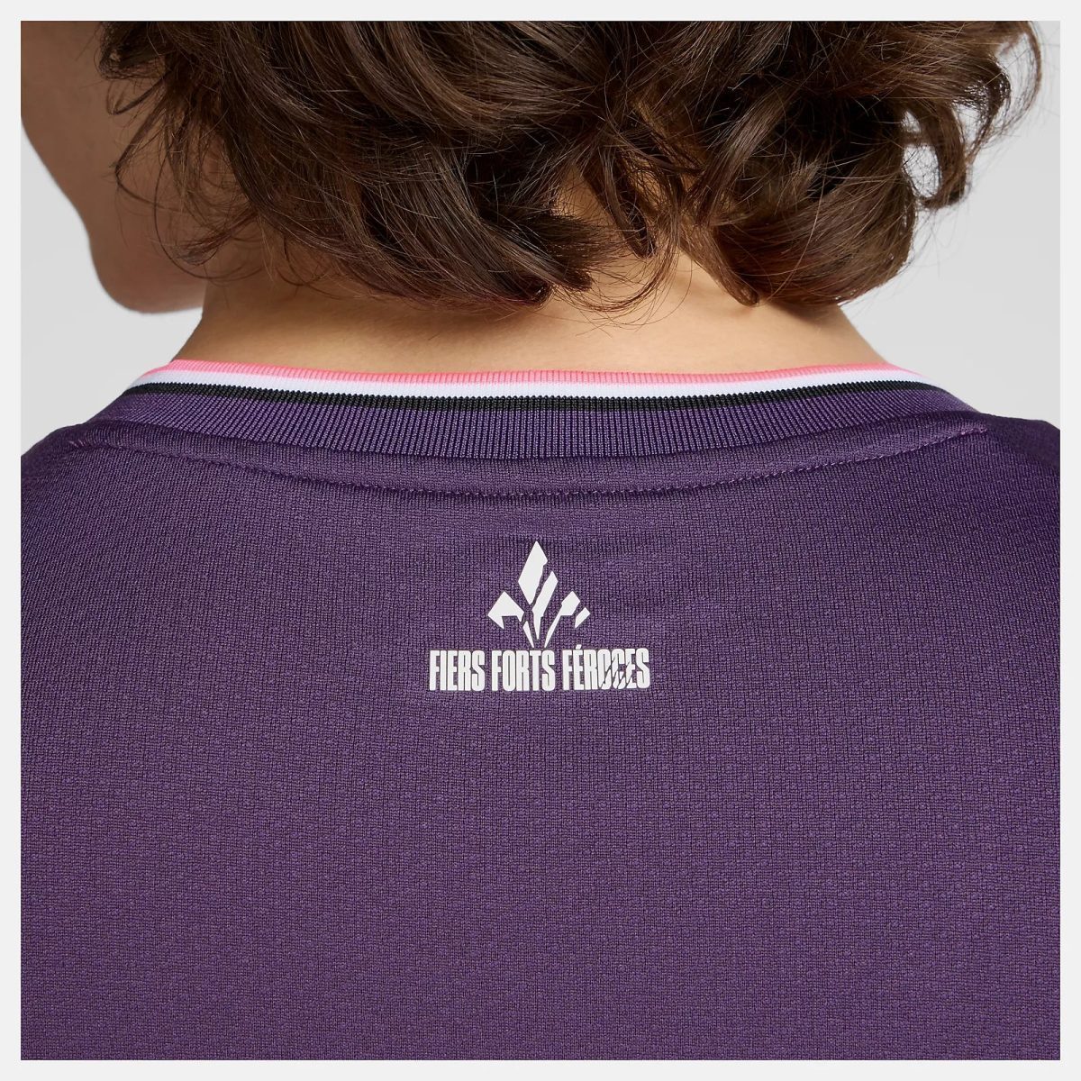 Back view of a person wearing a purple knit shirt with a white geometric logo and the words FIERS FORTS FÉROZES on the back neck area.