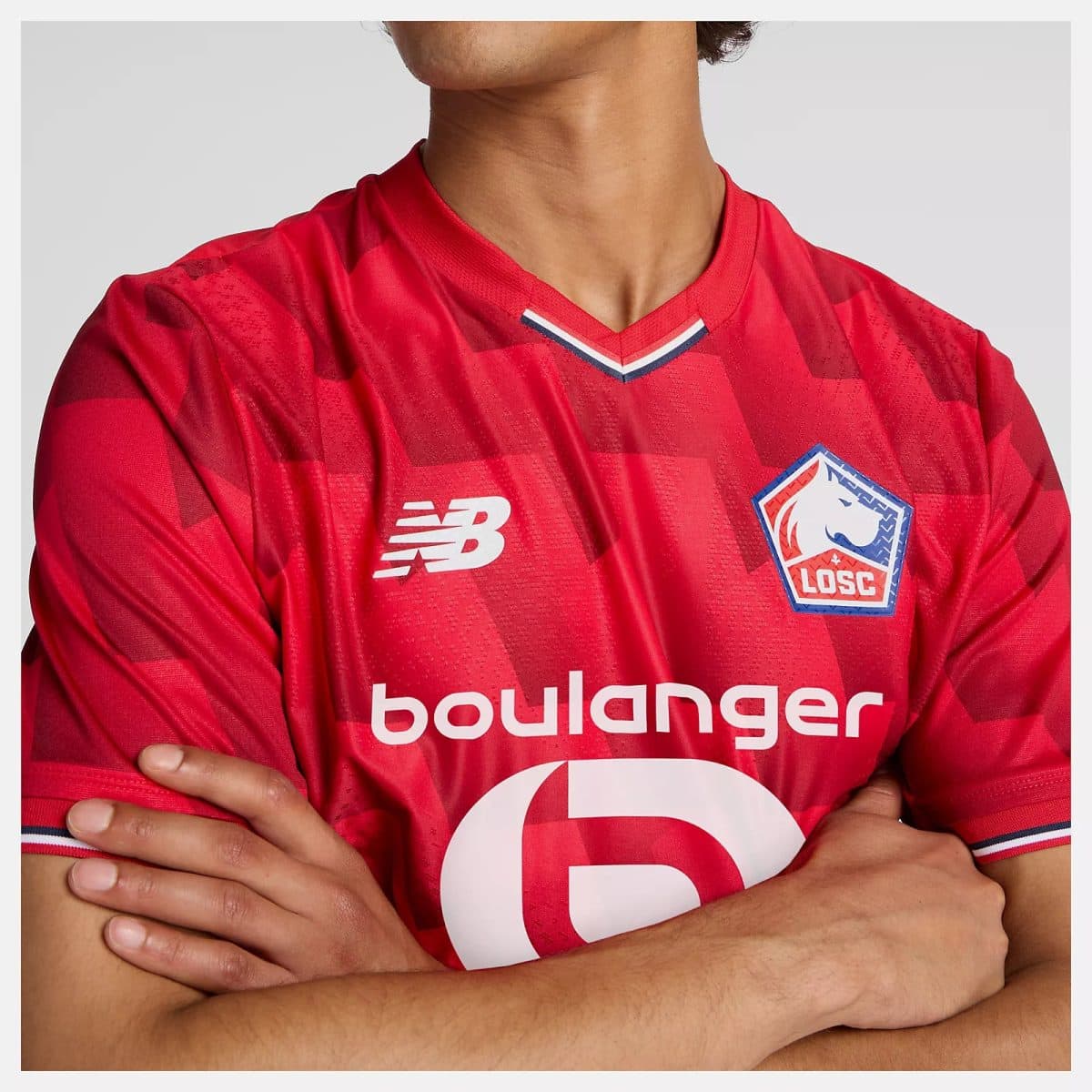 Close-up of a red Lille OSC soccer jersey with crest, New Balance logo, and crossed arms visible on the chest area.