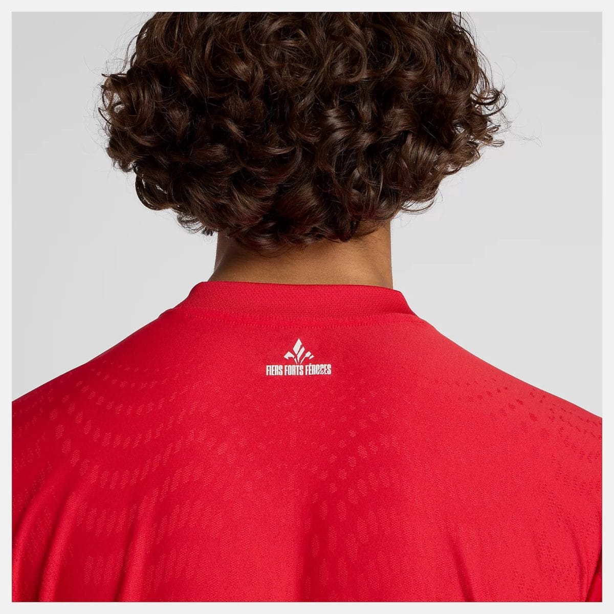 Back view of a person with curly hair wearing a red athletic jersey featuring a small white logo on the upper back.