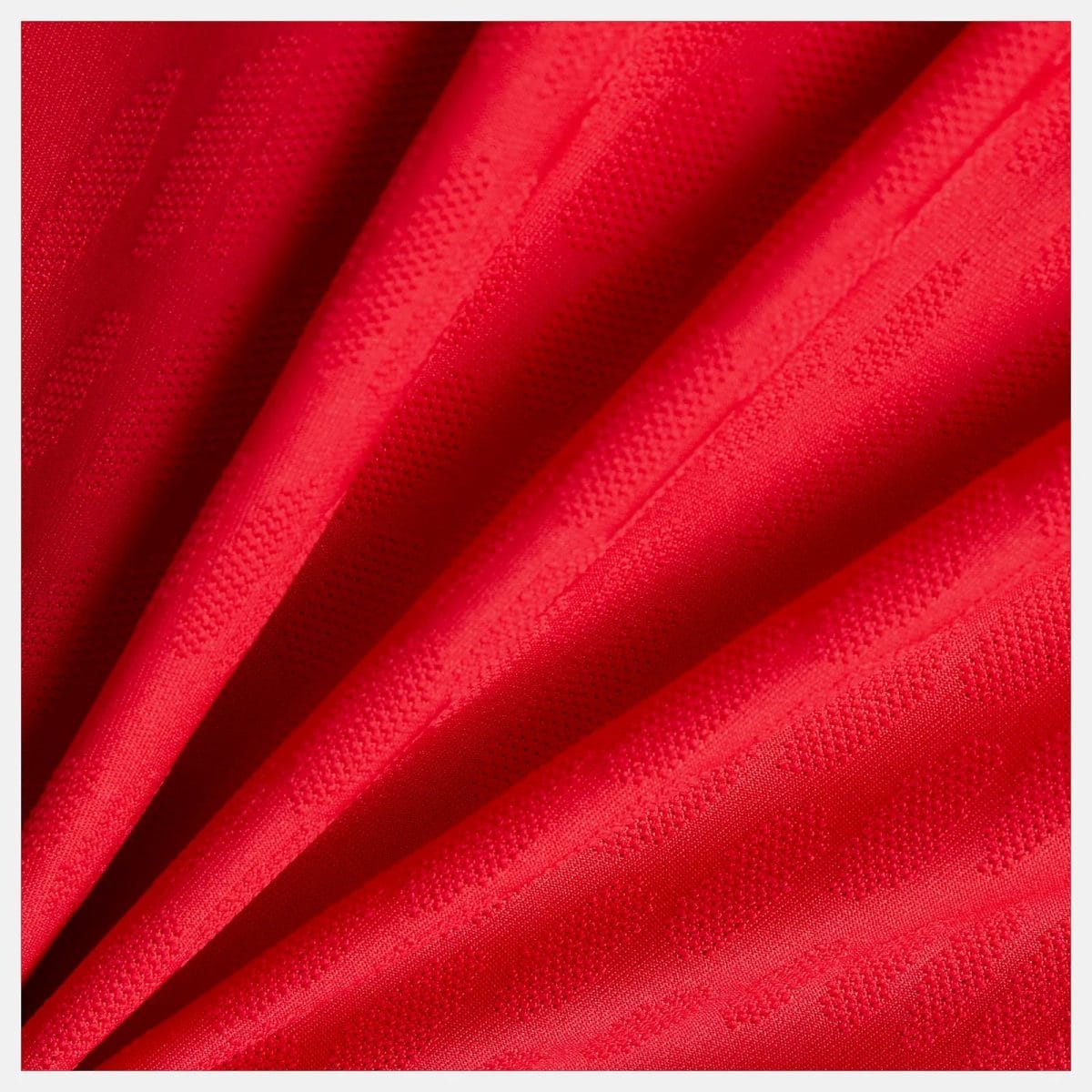 Close-up of bright red fabric with diagonal folds and a dotted textured weave.
