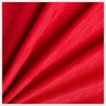 Close-up of bright red fabric with diagonal folds and a dotted textured weave.