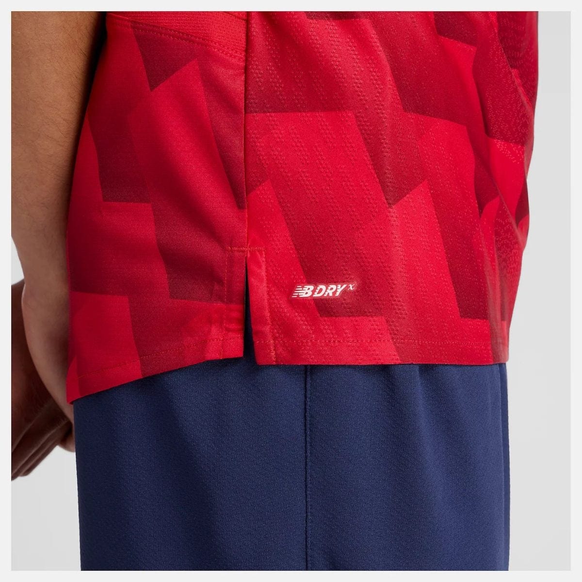 Close-up of red geometric-patterned athletic shorts with a small white NB DRY X logo at the hem.