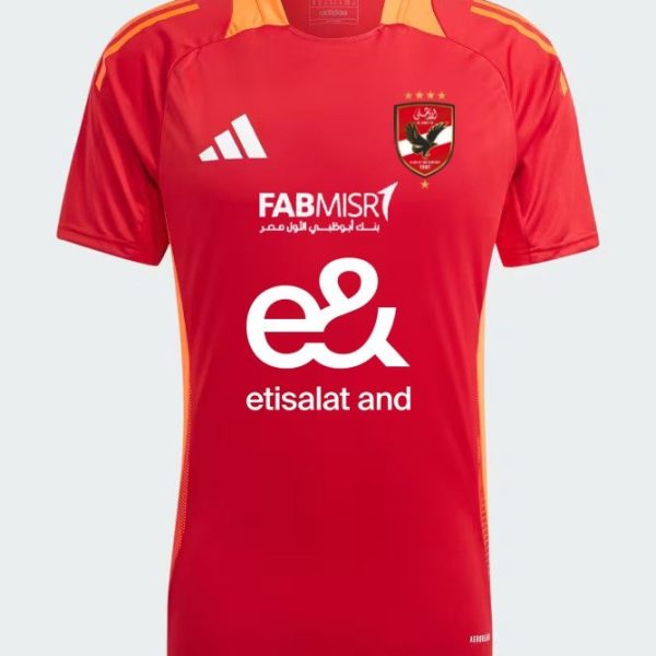 Red soccer jersey with orange shoulder accents and sponsor logos, featuring a crest on the left chest and Adidas logo on the right.