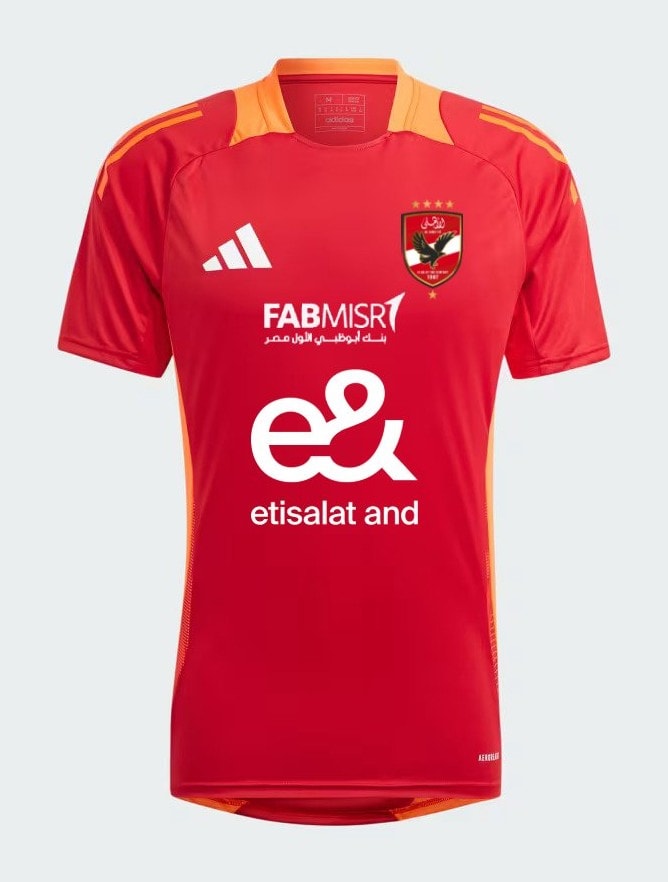 n6Mzy6RnRYmkkJg | UAE SPORT STORE Red soccer jersey with orange shoulder accents and sponsor logos, featuring a crest on the left chest and Adidas logo on the right.