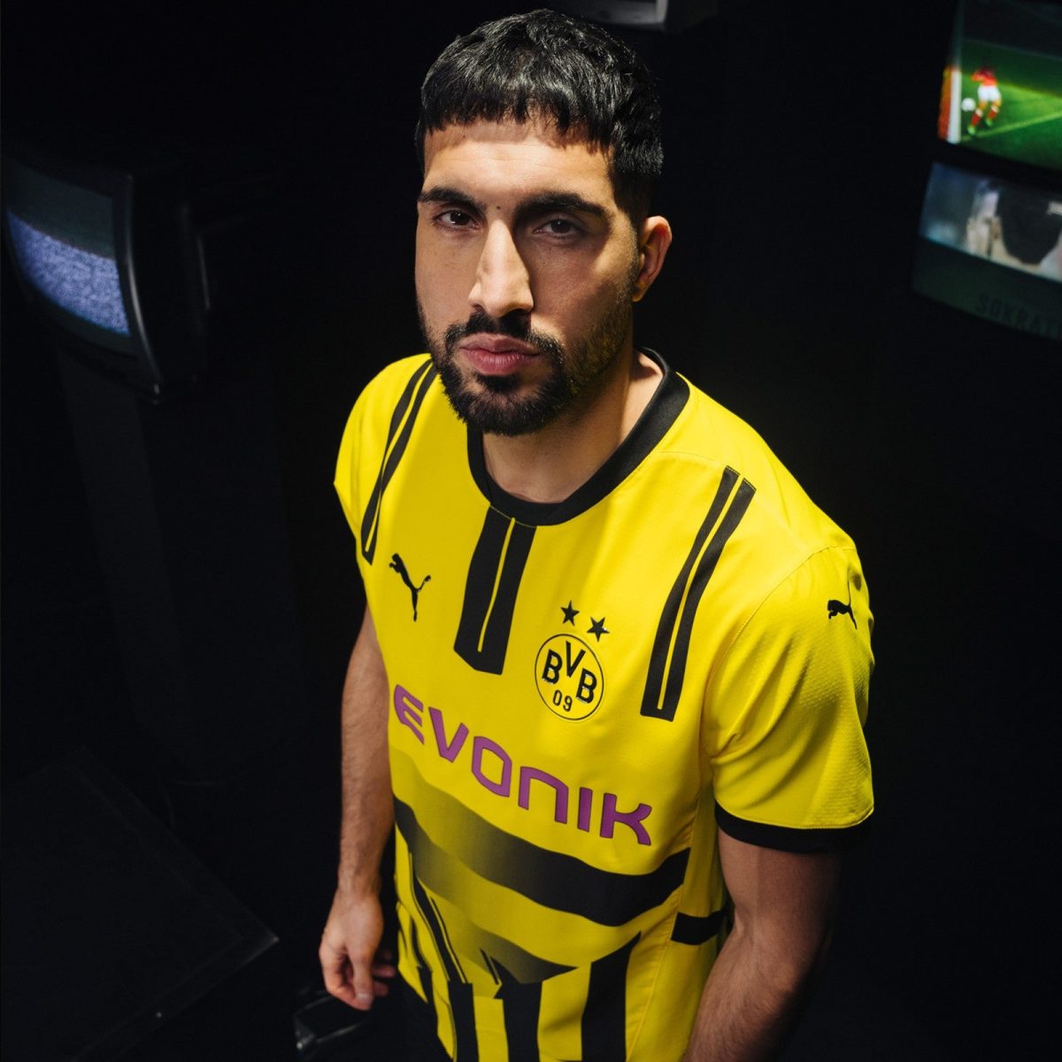 Portrait of a man with a beard wearing a yellow Borussia Dortmund jersey, looking at the camera in a dark setting, with team crest visible on chest.