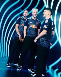 Three teammates in matching blue jerseys with Red Bull logos pose together, smiling against a neon blue, wave-pattern backdrop.