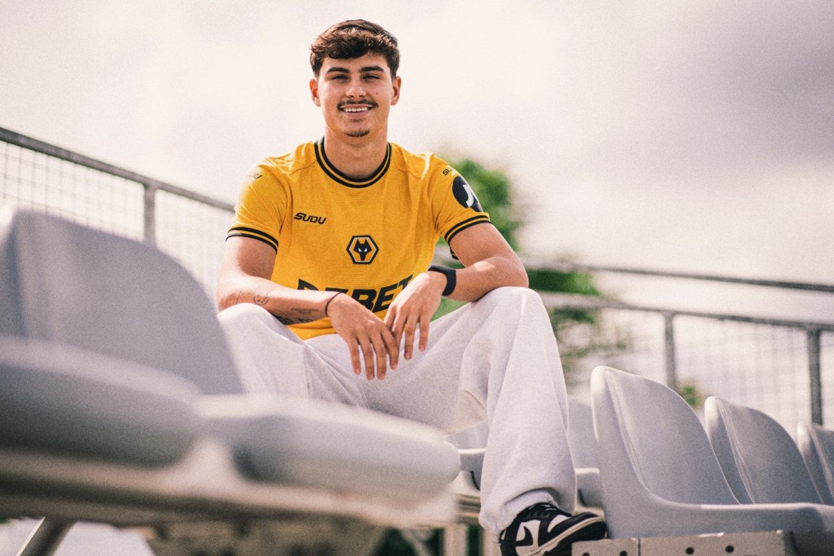 Young man in a yellow athletic jersey sits on stadium bleachers, smiling at the camera with a railing behind him.