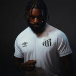 Portrait of a bearded man in a white football jersey with the S.F.C crest and Umbro logo against a dark background, looking downward.