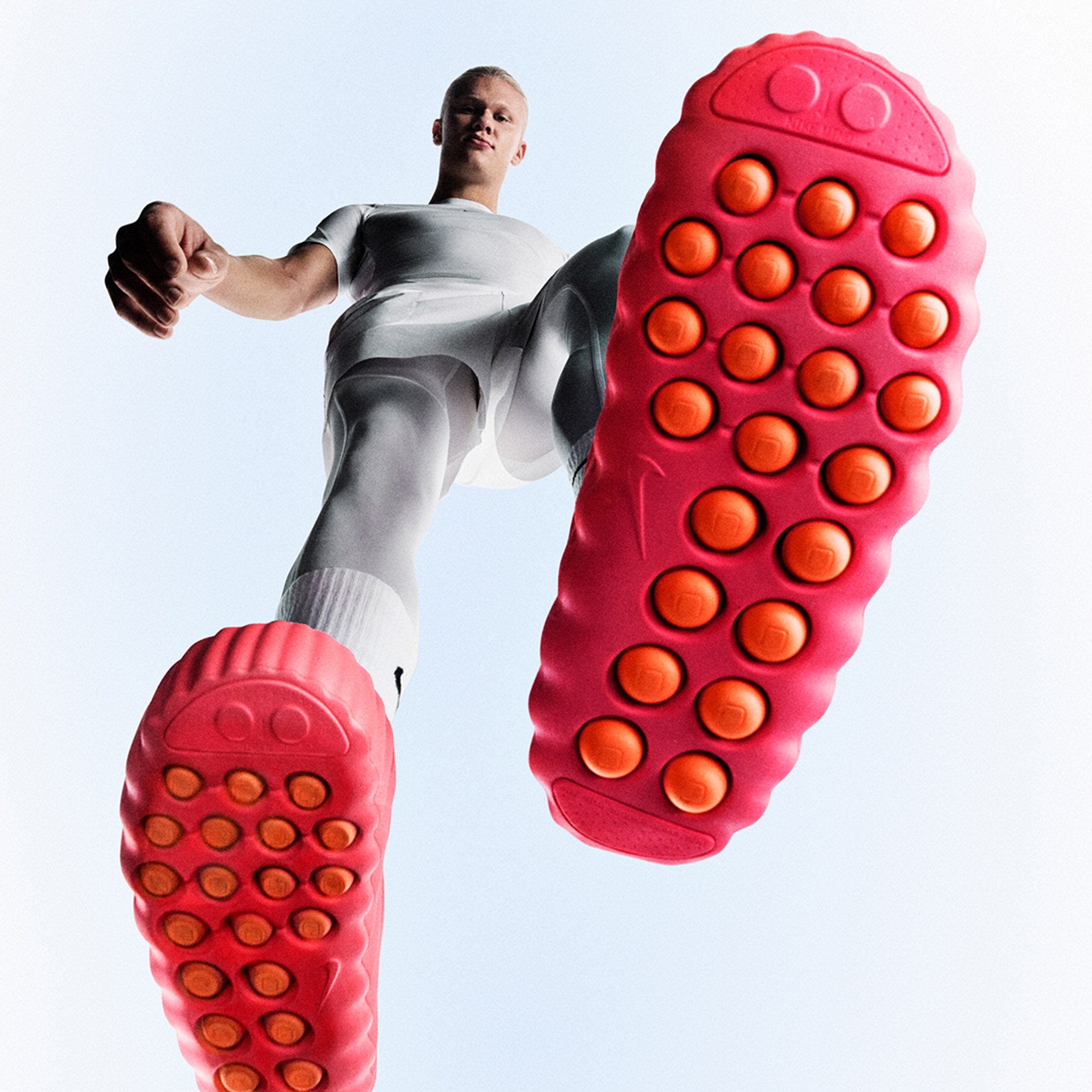 Close-up of a bright pink athletic shoe sole with orange studs against a light blue background.